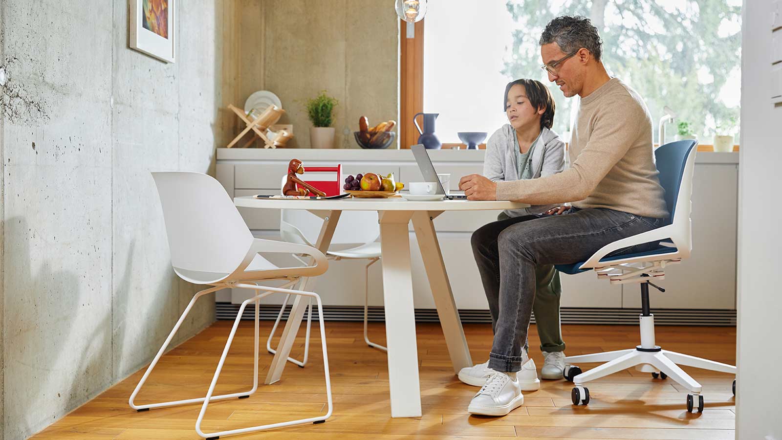 Bürostuhl Aeris Numo Task am Küchentisch mit Mann auf Stuhl und Kind weißes Gestell Std. blaugrau farbene Polster
